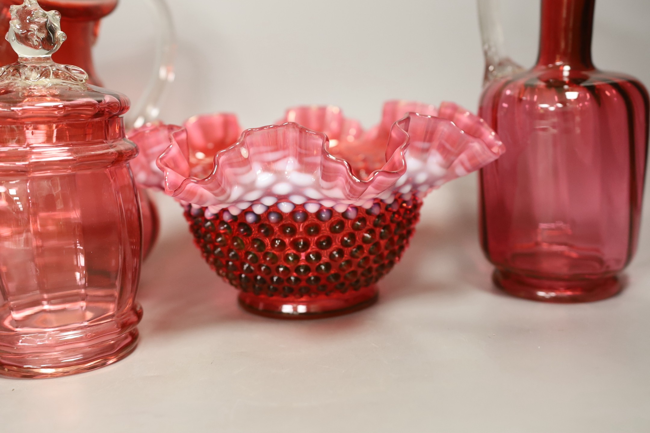 A pair of cranberry glass decanters, a jug, a fluted vase and a biscuit box and cover- decanters and stoppers 28cms high.